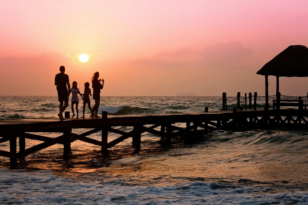 family-pier-man-woman-39691-39691 Silhouetted family enjoys a stroll on the beach pier at a vibrant sunset over the ocean waves.